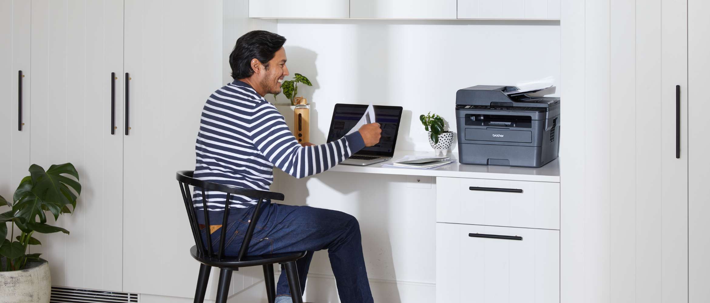 A man is sitting in his hybrid office working remotely from home. He is reviewing a document printed from a Brother printer.