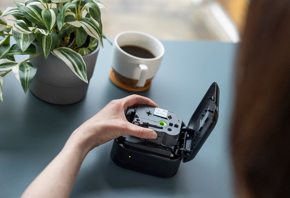 Plant and a coffee cup on a table with a hand holding an open P-touch Cube labeliing machine