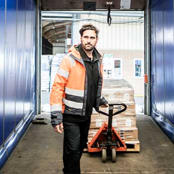 Man som bär orange varselväst pälsen som drar vagn med lådor