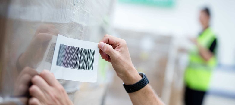  Etikett med streckkod fästs på en pall med lådor som har plast runt sig på ett lager